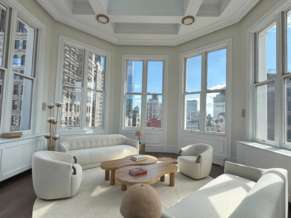 A pair of curved boucle lounge chairs and a sofa in a bay-windowed parlor above the city