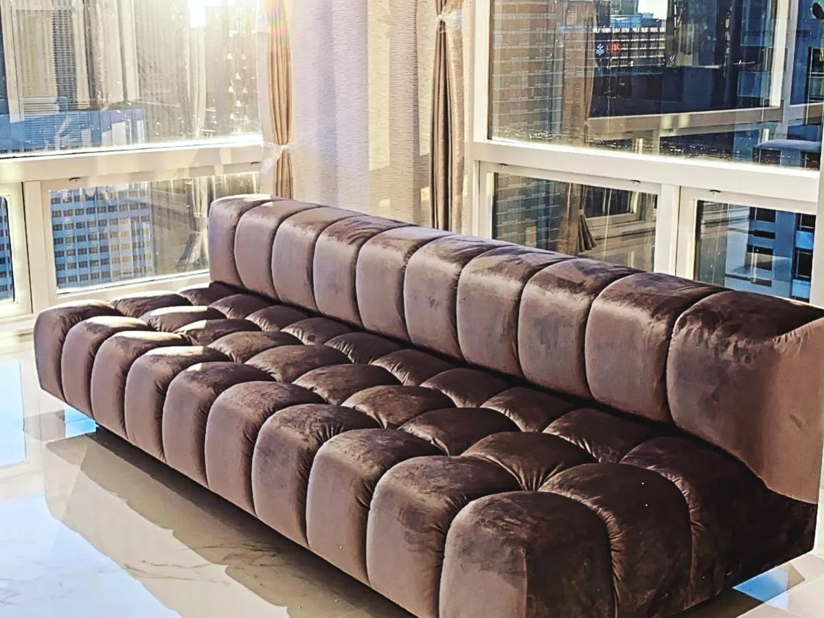 A long channel-tufted chocolate velvet banquette along a wall of city windows