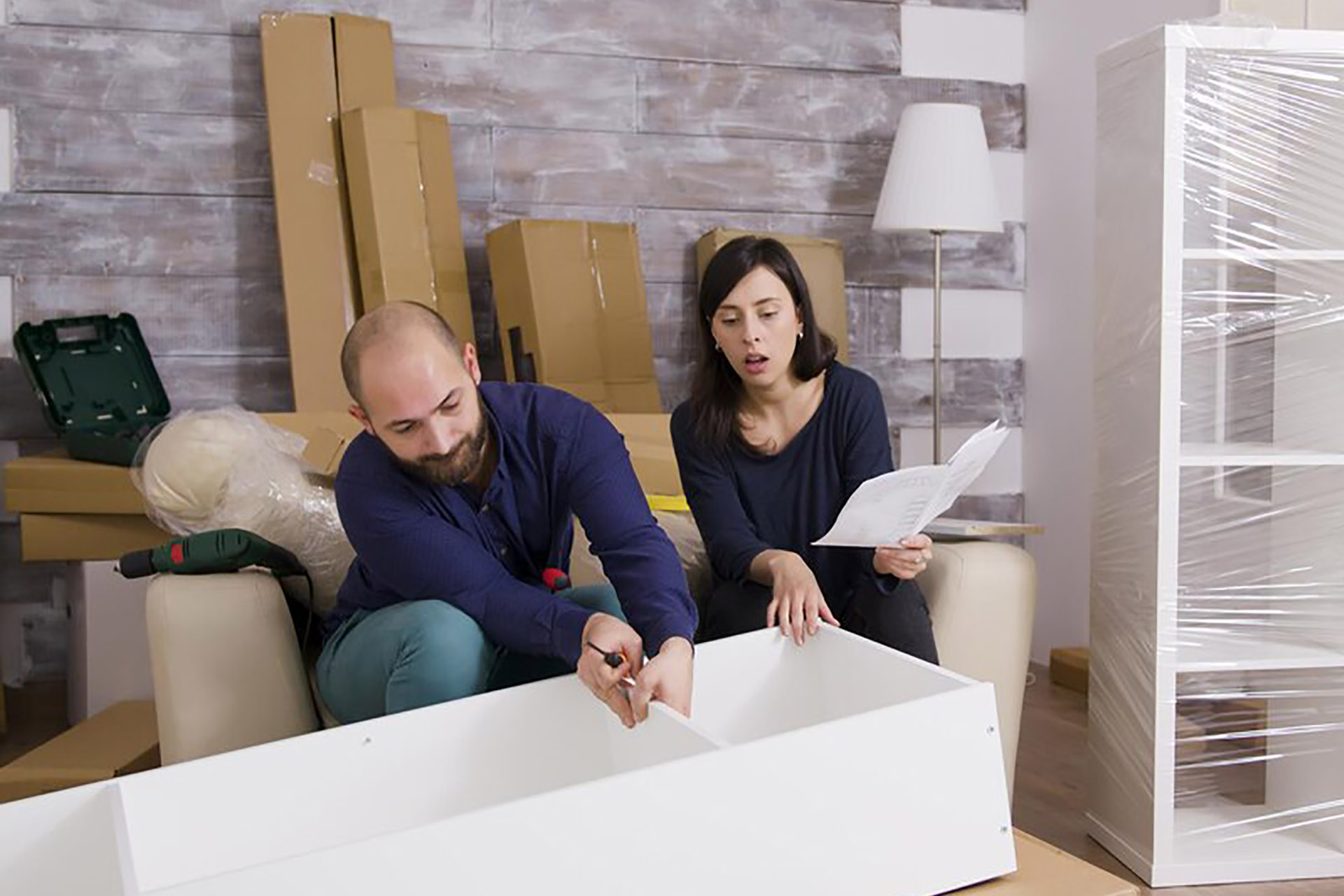 people assembling furniture surrounded by moving boxes, tools, and instructions—setting up a new space.